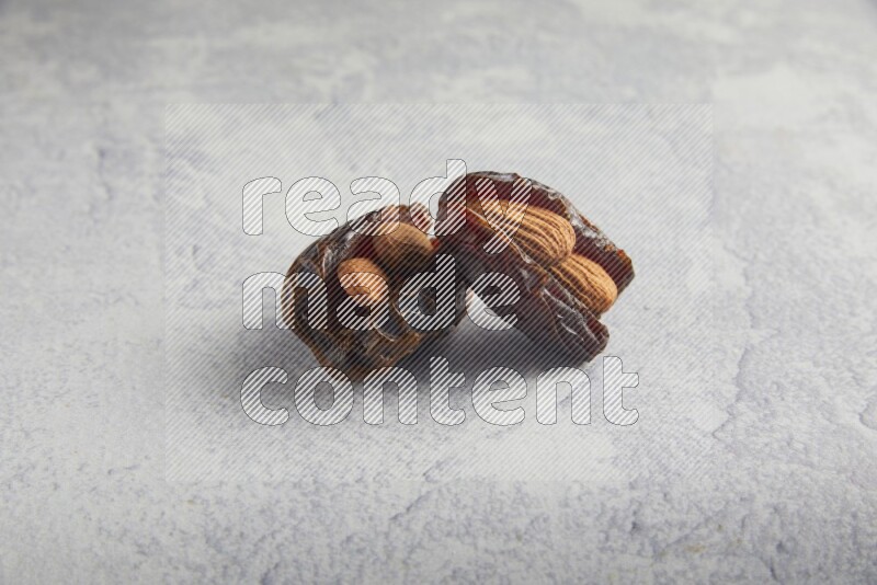 two almond stuffed madjoul dates on a light grey background