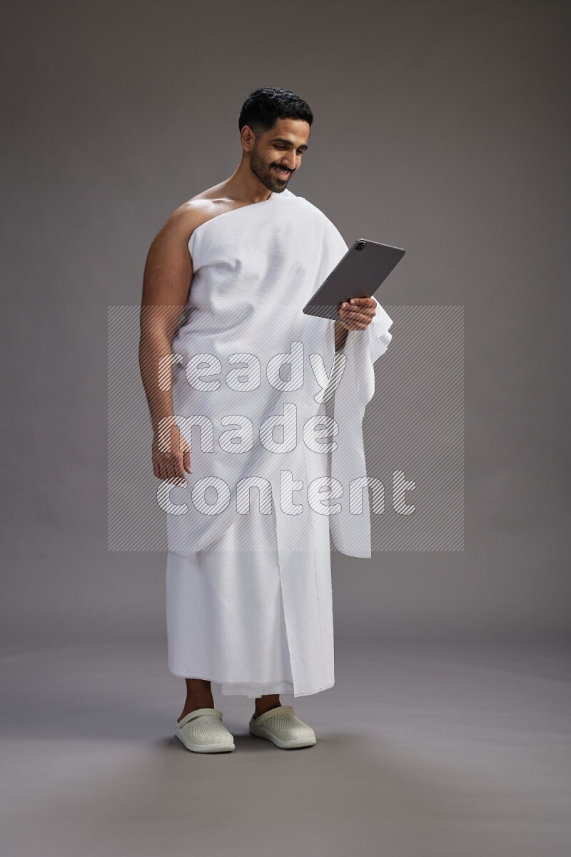 A man wearing Ehram and holding a tablet on gray background