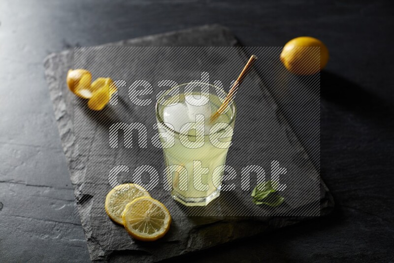 A glass of lemon juice with a straw on black background
