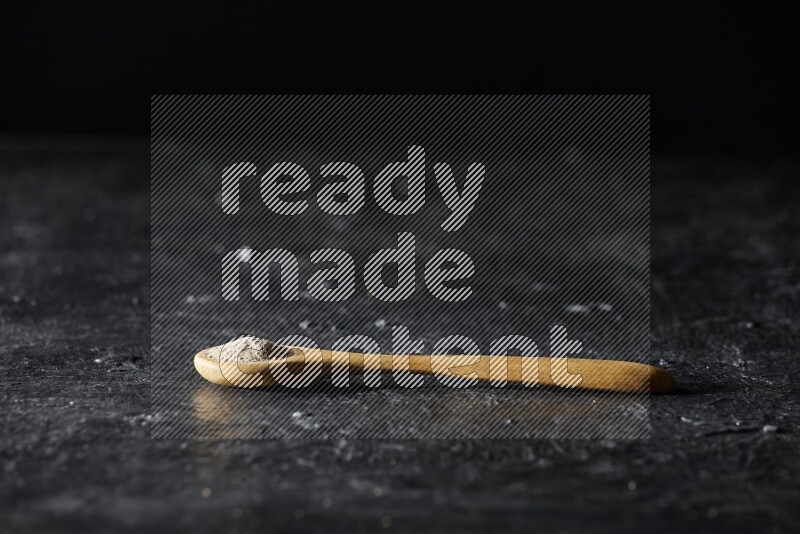 A wooden spoon full of white pepper powder on textured black flooring
