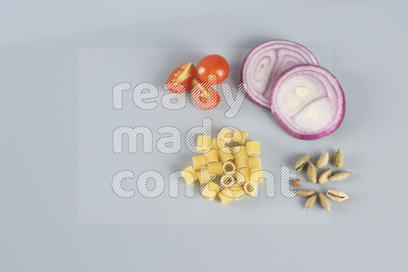 Raw pasta with different ingredients such as cherry tomatoes, garlic, onions, red chilis, black pepper, white pepper, bay laurel leaves, rosemary, cardamom and mushrooms on light blue background