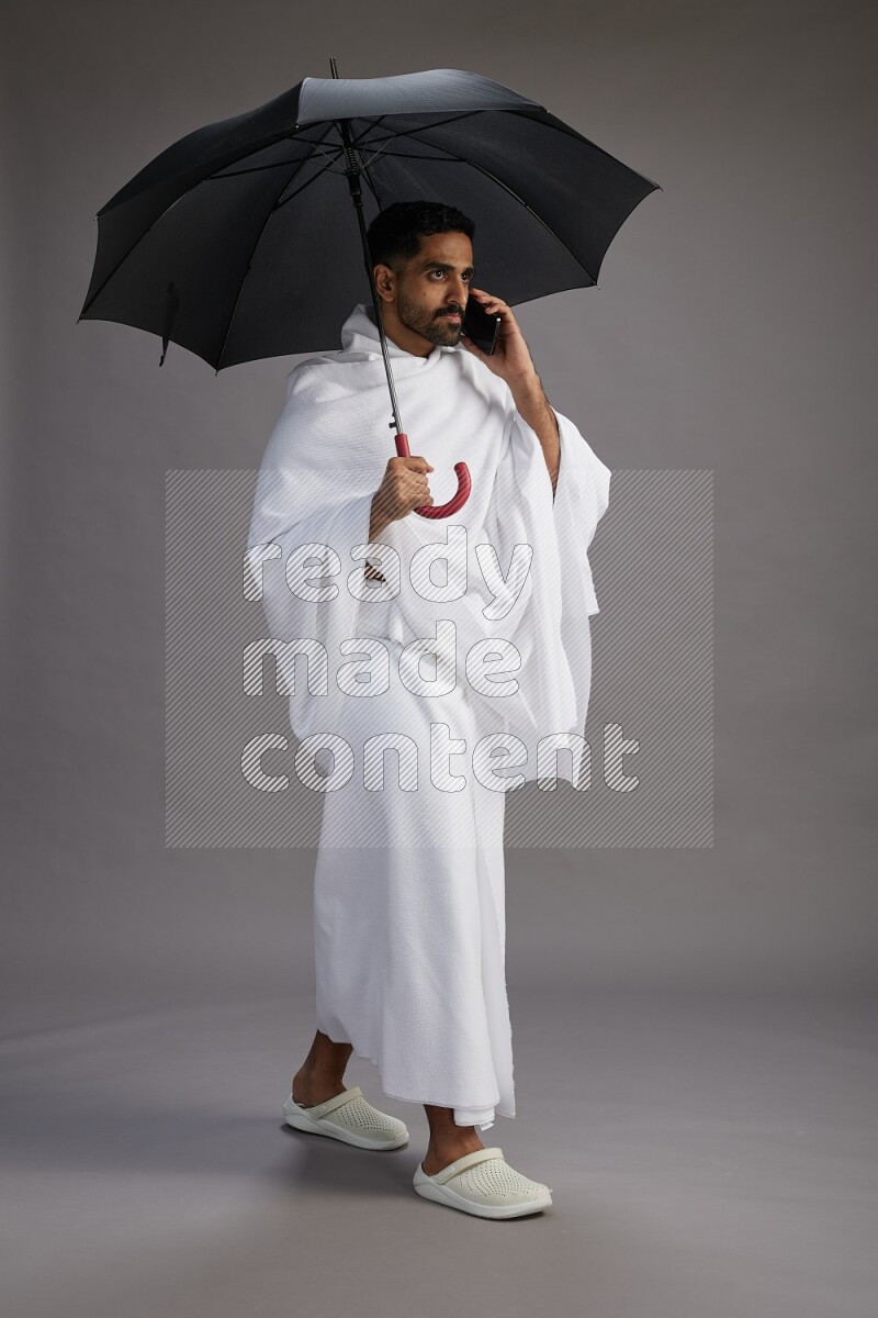 A man wearing Ehram Standing holding umbrella on gray background