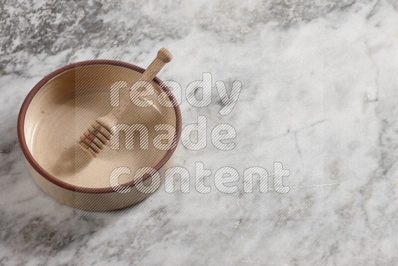 Beige Pottery oven bowl with wooden honey handle on the side with grey marble flooring, 65 degree angle