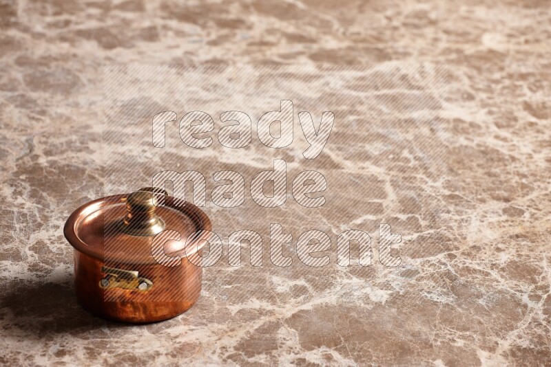 A small copper pot on beige marble background