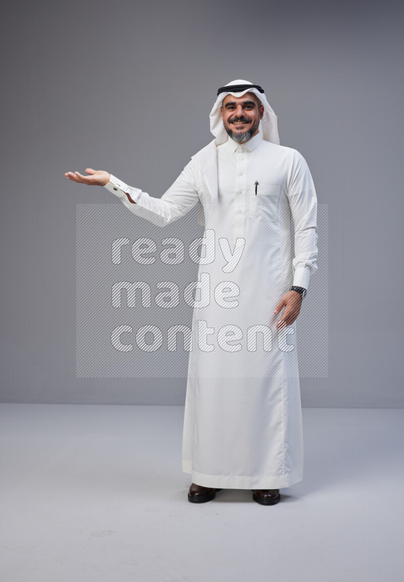 Saudi man Wearing Thob and white Shomag standing interacting with the camera on Gray background