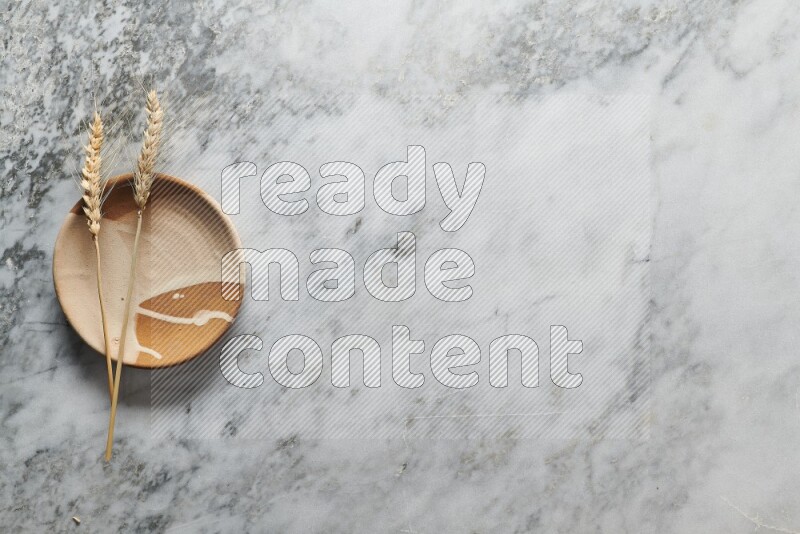 Wheat stalks on multicolored pottery plate on grey marble background