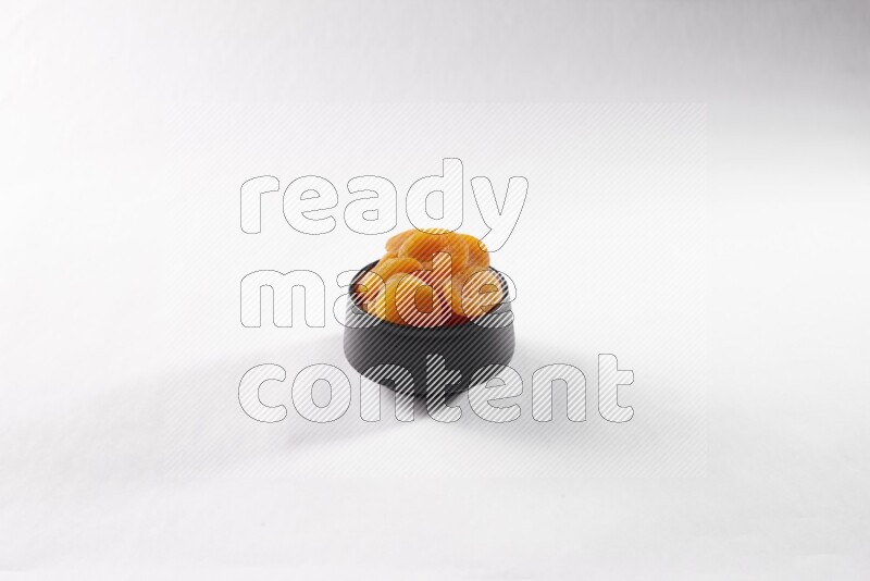 Dried apricots in a black pottery bowl on white background