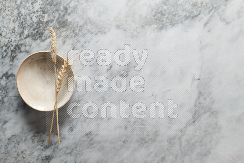 Wheat stalks on beige pottery plate on grey marble background