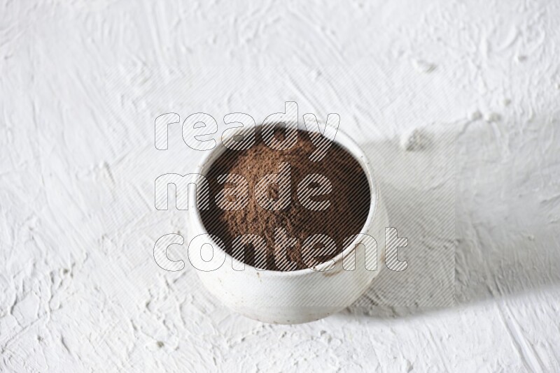 A beige ceramic bowl full of cloves powder on a white flooring