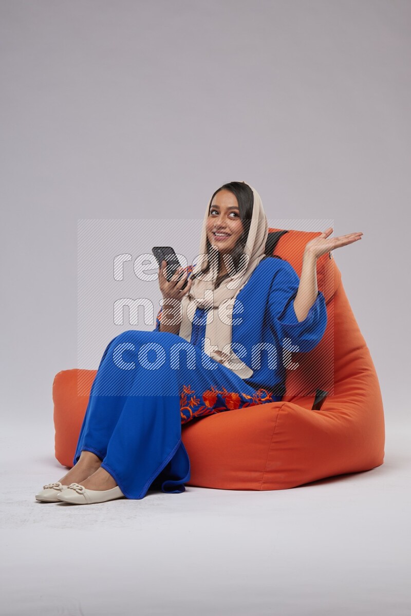 A Saudi woman sitting on an orange beanbag and texting on phone