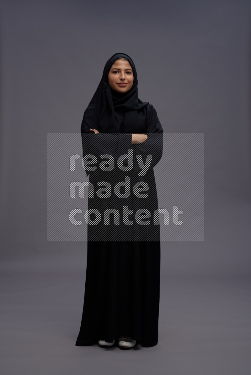Saudi woman wearing Abaya standing with crossed arms on gray background