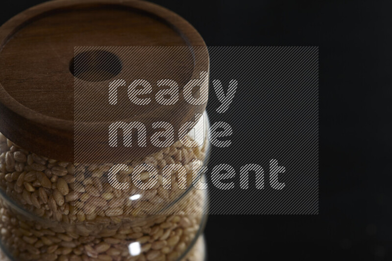 Hulled wheat in a glass jar on black background