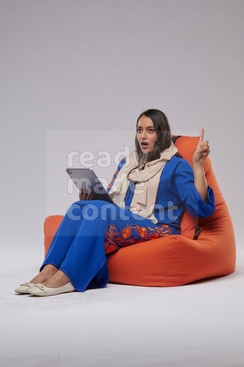 A Saudi woman sitting on an orange beanbag and working on tablet