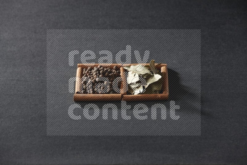 مربعان من أعواد القرفة ممتلئان ببهار الفلفل الحلو وأوراق الغار علي خلفية سوداء