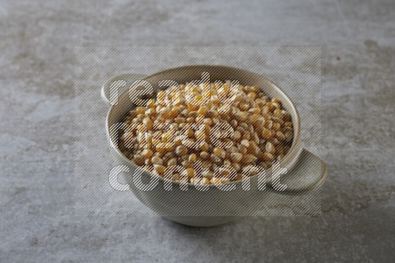 corn kernel in a off-white handheld ceramic bowl on a grey textured countertop