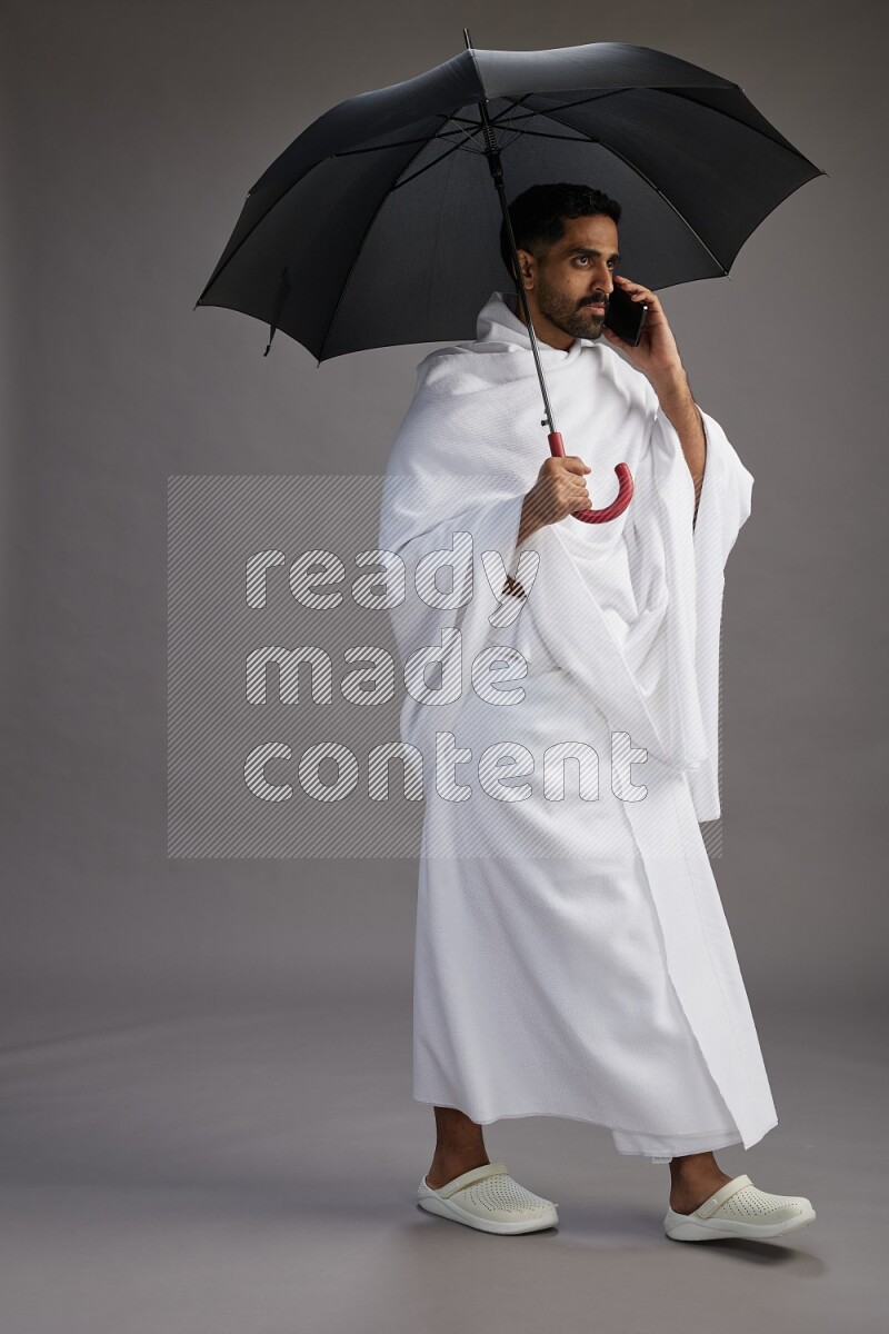 A man wearing Ehram Standing holding umbrella on gray background