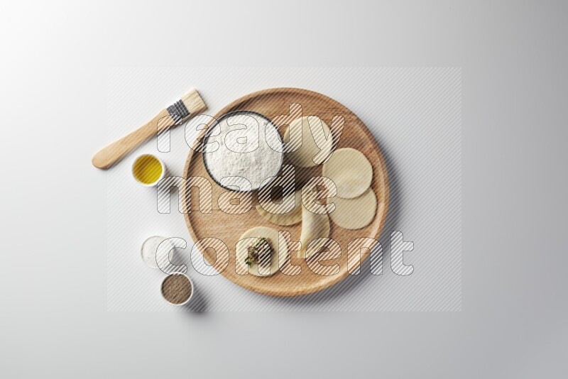 two closed sambosas and one open sambosa filled with meat while flour, salt, black pepper and oil with oil brush aside in a wooden dish on a white background