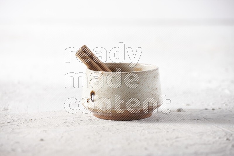 Ceramic beige bowl full of cinnamon powder with a cinnamon stick on a textured white background