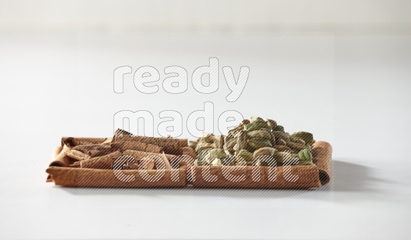 مربعان من أعواد القرفة ممتلئان بقطع من القرفة وحبوب الهيل علي خلفية بيضاء