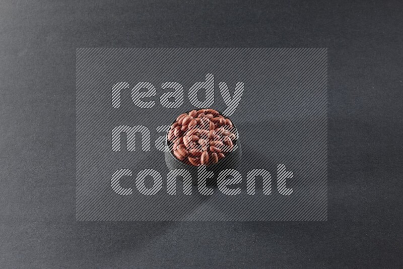 A black pottery bowl full of red skin peanuts on a black background in different angles