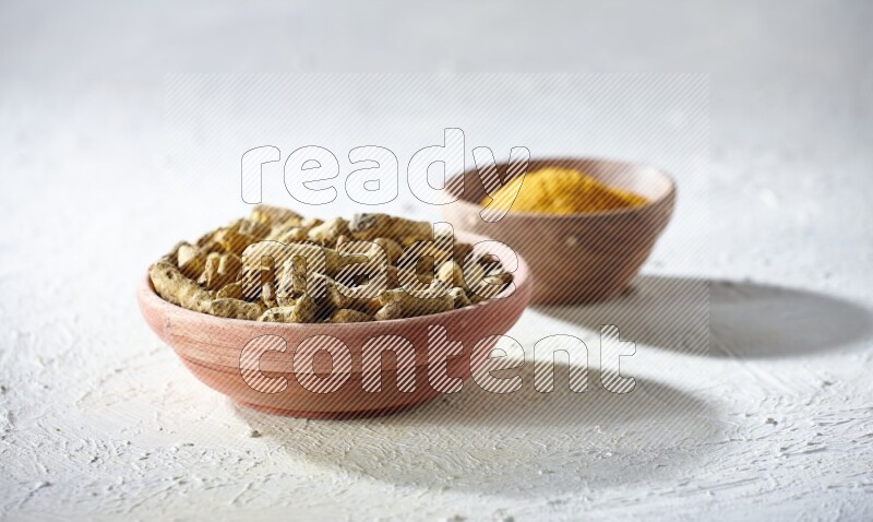 2 wooden bowls, one full of turmeric powder and the other full of dried turmeric whole fingers on a textured white flooring