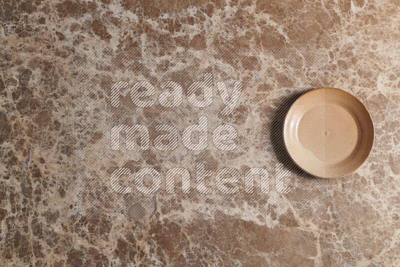 A beige pottery plate on beige marble background