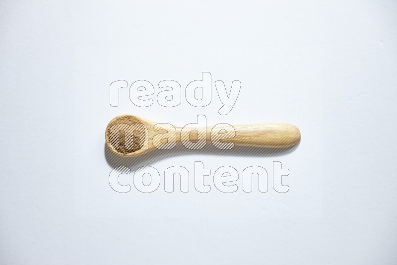 ملعقة خشبية ممتلئة ببودرة الكمون على خلفية بيضاء