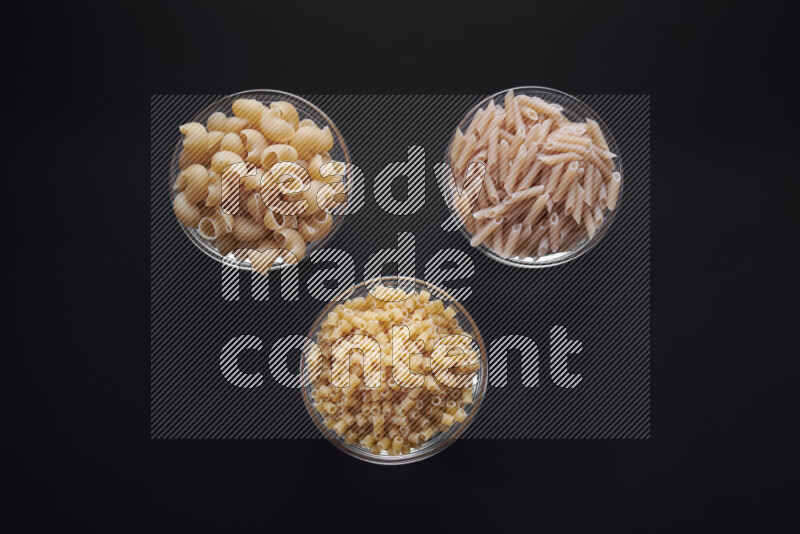 Different pasta types in glass bowls on black background