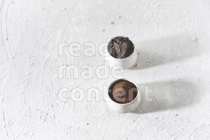 2 Beige ceramic bowls, one full of cloves and the other full of powder on textured white flooring