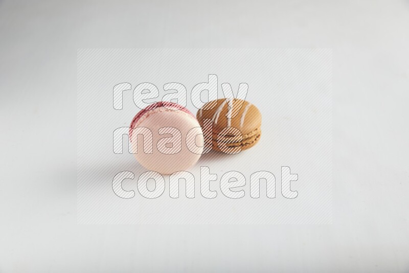 45º Shot of of two assorted Brown Irish Cream, and Pink Litchi Raspberry macarons on white background