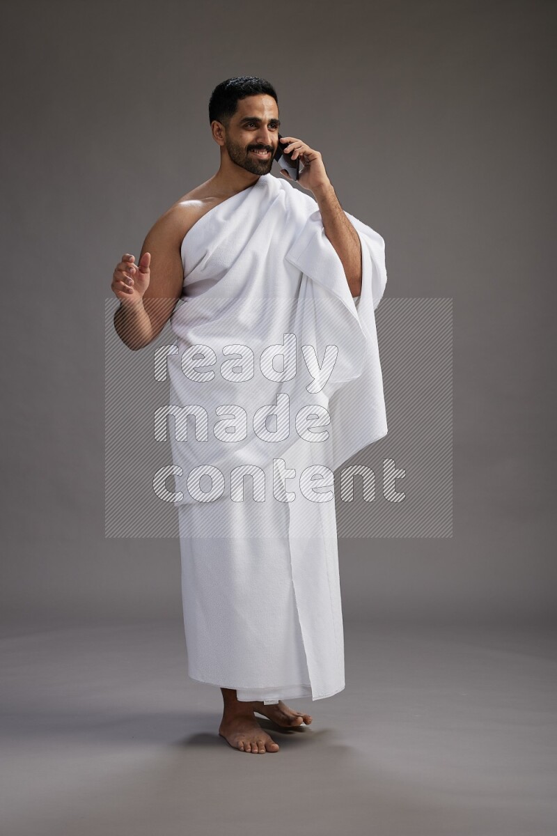 A man wearing Ehram Standing talking on phone on gray background