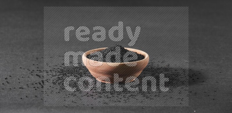 وعاء خشبي ممتلئ ببذور حبة البركة محاط ببعض البذور علي خلفية سوداء