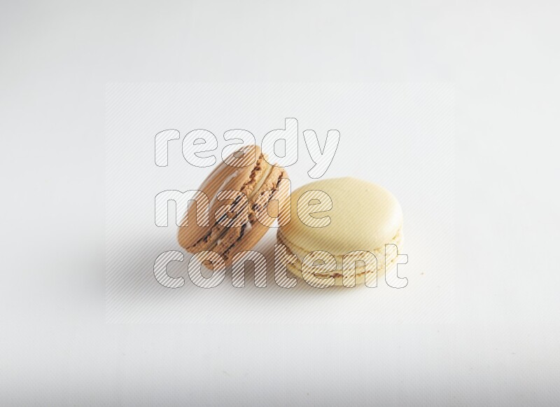 45º Shot of of two assorted Brown Irish Cream, and Yellow Vanilla macarons on white background