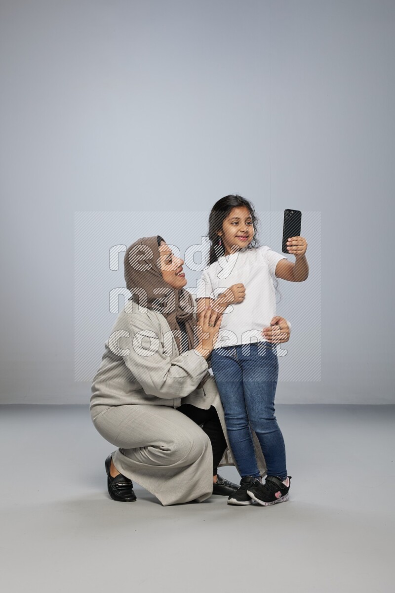 A girl standing taking selfie with her mother on gray background