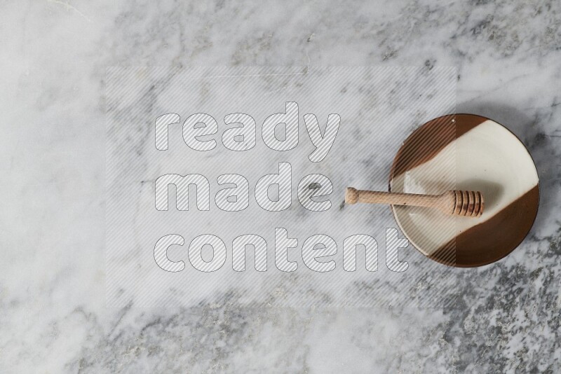 Multicolored pottery plate with wooden honey dipper in it on grey marble background