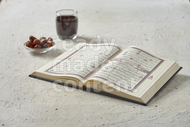 Quran with dates, prayer beads and different drinks all placed on textured white background