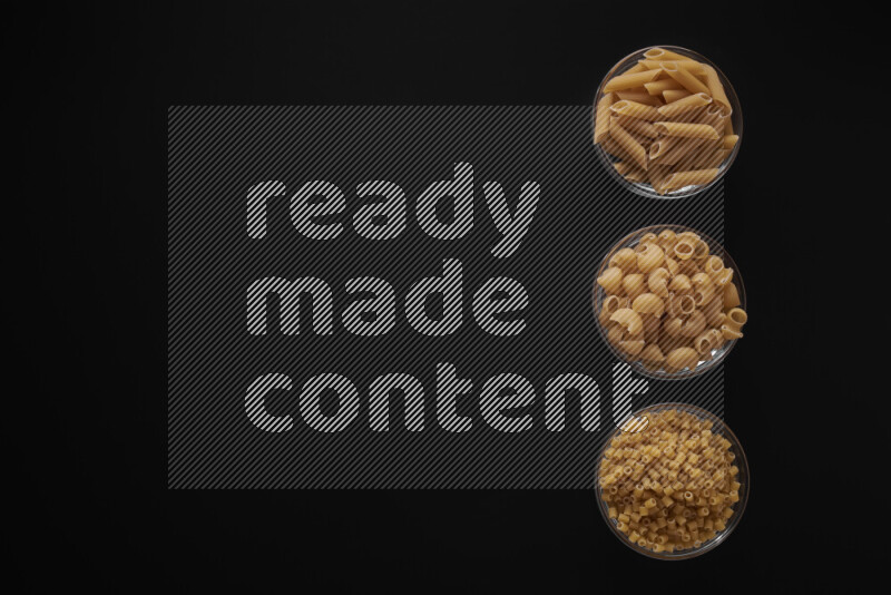 Different pasta types in 3 glass bowls on black background