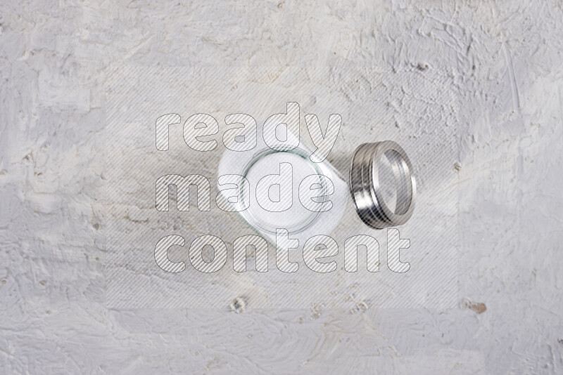 A glass jar full of fine table salt on white background