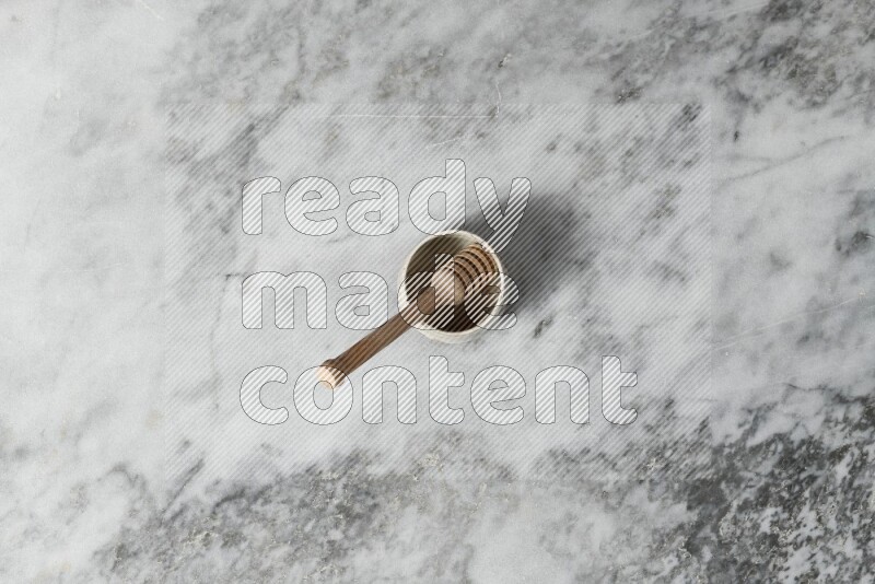 Black pottery bowl with wooden honey dipper in it on grey marble background