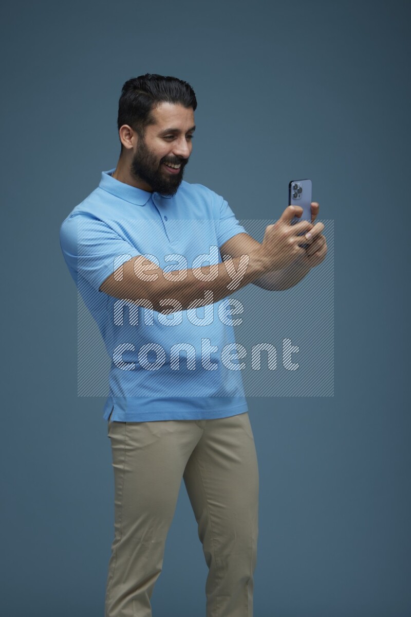 Man taking a picture with his phone  in a blue background wearing a Blue shirt