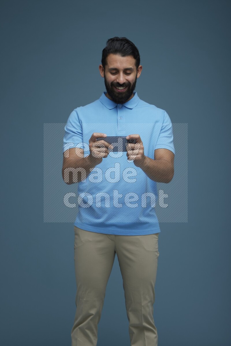 Man playing a game on his phone in a blue background wearing a Blue shirt