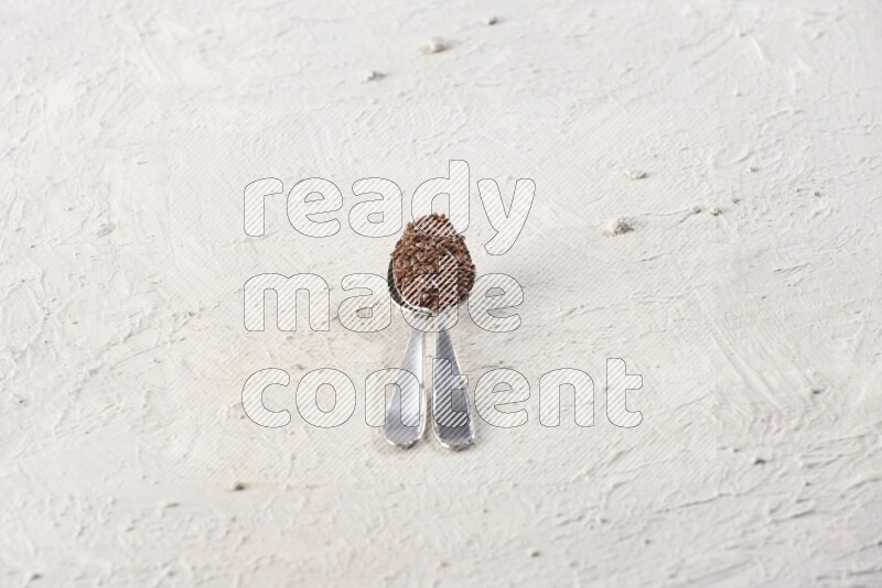 2 metal spoons full of flax seeds on a textured white flooring