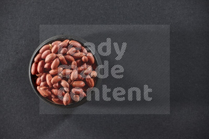 A black pottery bowl full of red skin peanuts on a black background in different angles