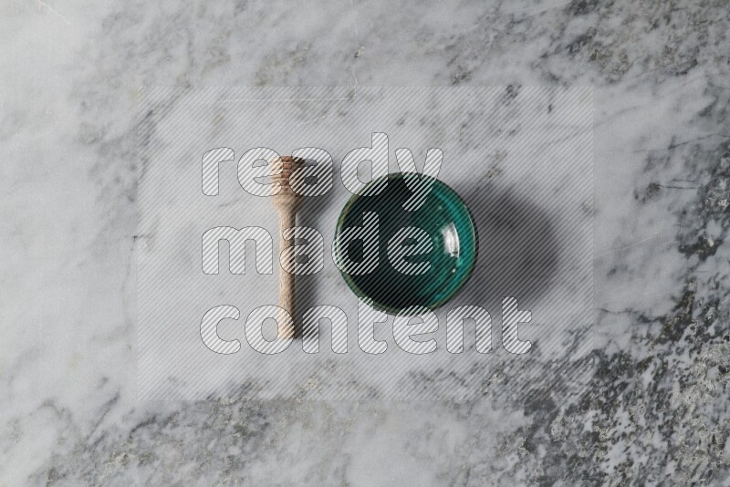 Dark green pottery bowl with wooden honey dipper on the side on grey marble background