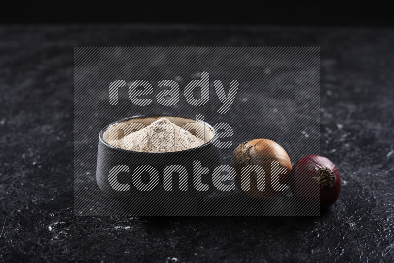 A black pottery bowl full of onion powder on black background