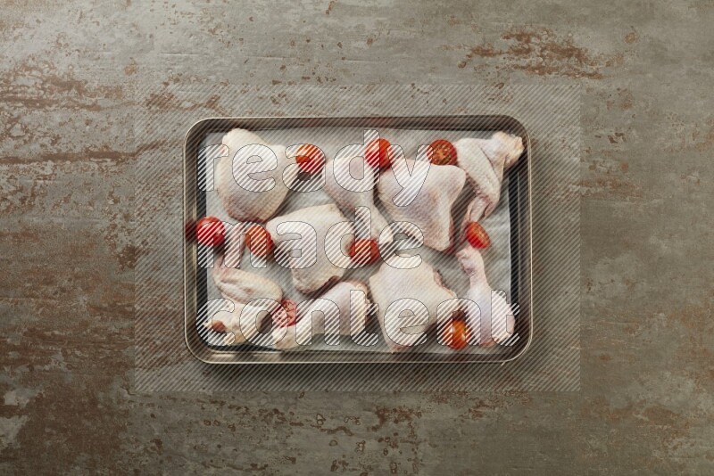 Mixed fresh chicken pieces in an oven tray on a textured rustic background