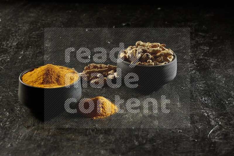 وعاءان من الفخار باللون الأسود، أحدهما ممتلئ ببودرة الكركم والآخر ممتلئ بأصابع كاملة من الكركم المجفف على خلفية سوداء