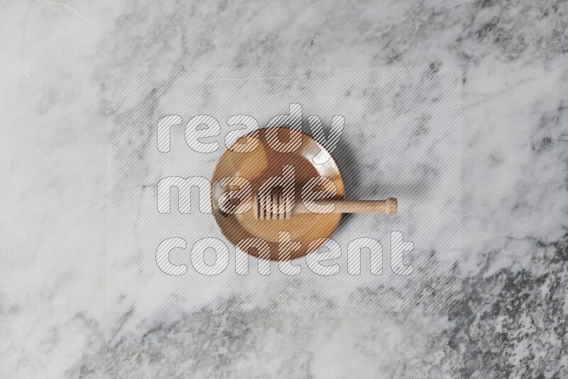 Multicolored pottery plate with wooden honey dipper in it on grey marble background