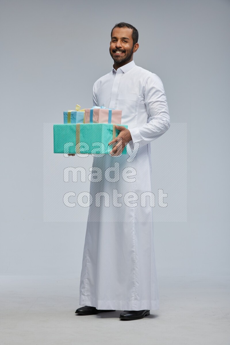 Saudi man Wearing thob standing holding gift box on Gray background