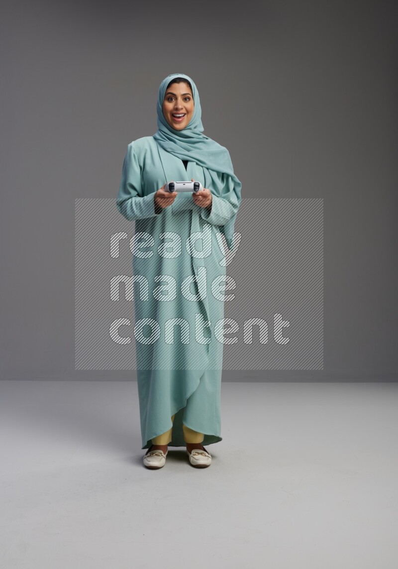 Saudi Woman wearing Abaya standing Playing Games on Gray background